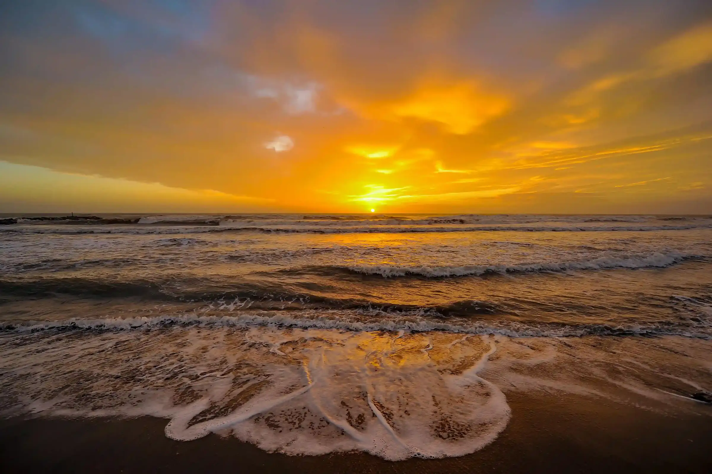 Golden sunset over the ocean, the sun low on the horizon and surf washing up a wide empty beach
